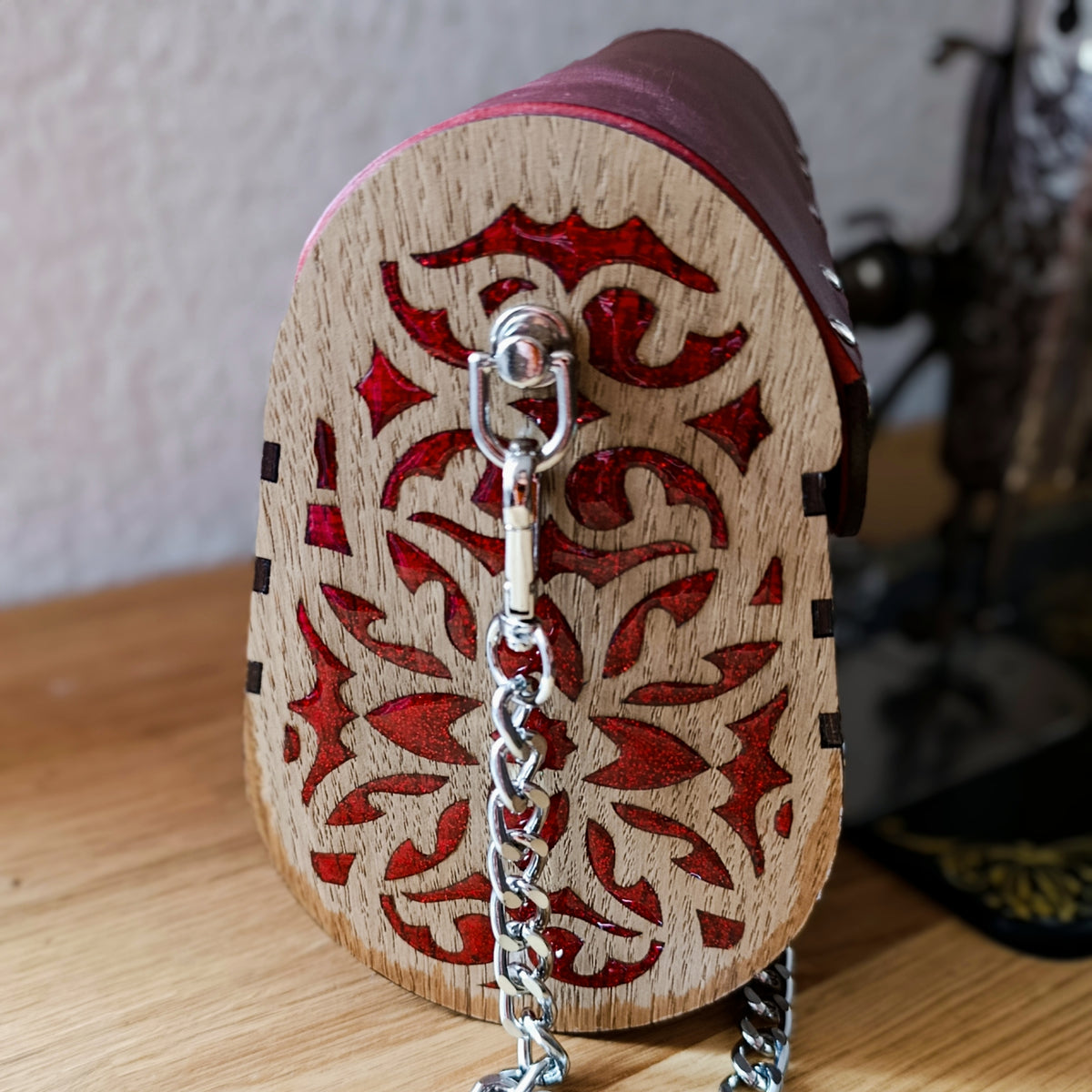 Côté de la pochette en bois gravé avec motifs remplis de résine rouge pailletée et attache de chaîne amovible en métal.